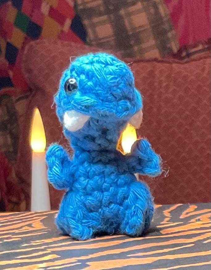 Blå dinosaur med hvide tænder foran et stearinlys